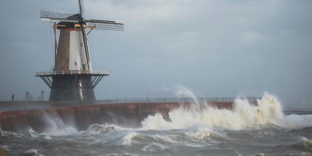 Windmolen op een kade waar golven overheen slaan